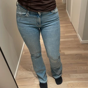 Bootcut ljusblå jeans med paljetter - Snygga ljusblå bootcut jeans med paljettdetaljer längst ner på benen och slitna kanter vid bensluten. Jeansen har klassisk femficksdesign, hög midja och är tillverkade i mjukt denimtyg. Perfekt för dig som vill ha lite extra bling i vardagen. Från Ginatricot Storlek: 158, jag brukar normalt ha S eller 36 och dessa passar mig.