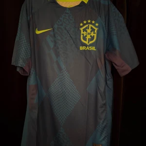 Blå Brasilien fotbollströja Nike - Snygg blå fotbollströja från Nike med Brasilien-logga och gula detaljer. Tröjan har korta ärmar och ett unikt mönster med bland annat leopard och rutor. Perfekt för dig som vill sticka ut på planen eller heja på landslaget.