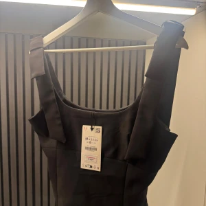 Svart ärmlös topp från Zara - Stilren svart topp från Zara med breda axelband och fyrkantig ringning.Toppen har en figurnära passform och är tillverkad i ett slätt material som ger en elegant look. Perfekt för dig som gillar minimalistisk stil och vill ha något klassiskt i garderoben.