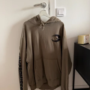 Gasp hoodie - Säljer en beige hoodie med svart tryck på bröstet och text längs ena ärmen. Tröjan har huva med snörning och en stor magficka framtill. Perfekt för en avslappnad och cool stil.