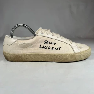Saint Laurent vita sneakers  - Snygga vita sneakers från Saint Laurent med handskriven logga på sidan. Nypris ~ 8000kr. Skorna har en klassisk låg profil, rund tå och platt sula. Tillverkade i canvas med detaljer i skinn och snörning framtill. Perfekta för en avslappnad och trendig look. Priset är inte hugget i sten! Skriv om frågor uppstår så svarar vi snabbt och ärligt.! //By, Olsén, Closet.