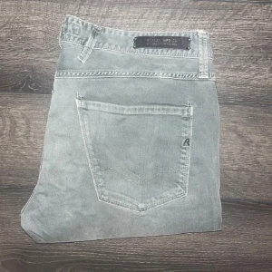 Replay jeans  - Snygga  jeans från Replay i modellen Anbass. Jeansen har en slim passform, klassisk femficksdesign och diskret Replay-logga på bakfickan. OBS färgen är khaki/grå beroende på ljus jag tar ej emot returer ifall man inte blir nöjd :) Midja 43 cm, längd 102cm.JAG SKICKAR EJ FLER BILDER NÄR JAG BÄR JEANSEN! för storleksguide hänvisar jag till måtten och för bättre inblick i passformen rekommenderar jag att googla på modellnamnet :) s3
