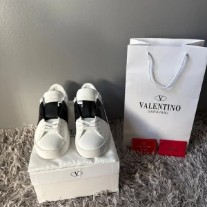Valentino Garavani vita sneakers - Snygga vita sneakers från Valentino Garavani med svart detalj på sidorna. Skorna har klassisk rund tå, platt sula och snörning framtill. Tillverkade i skinn för en lyxig känsla. Perfekta för dig som vill ha en stilren och exklusiv look.