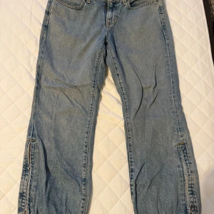 ljusblå jeans - Säljer ett par ljusblå jeans från GAP med låg midja och croppad passform. Jeansen har raka ben med resår och knappdetalj vid benslut samt klassiska fickor fram och bak. Perfekta för en chill och avslappnad stil.