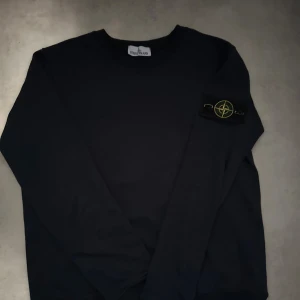 Mörkblå Stone Island sweatshirt - Säljer en mörkblå sweatshirt från Stone Island med den klassiska loggan på vänster ärm. Tröjan har rund halsringning och långa ärmar. Tillverkad i mjuk bomull för en skön och avslappnad stil.