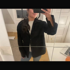 Svart manchesterskjorta oversized - Svart skjorta i manchester med klassisk krage, bröstficka och knäppning framtill. Modellen är oversized med långa ärmar och avslappnad passform. Perfekt att slänga över en t-shirt för en chill look. Passar kanon som jacka