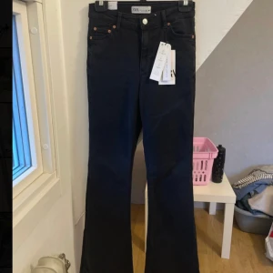 Svarta bootcut jeans från Zara, stl 34 - Snygga svarta bootcut jeans från Zara i storlek 34. Jeansen har klassisk femficksdesign, hög midja och utsvängda ben. Tillverkade i ett stretchigt bomullsmaterial för skön passform. Perfekta för dig som gillar en trendig siluett.