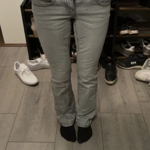 Grå bootcut jeans från Gina Tricot - Snygga ljusgrå jeans från Perfect Jeans i bootcut-modell. Jeansen har klassiska fickor fram och bak, dekorativa knappar och markerade sömmar. Använt endast få gånger. orginalpris 500kr. Perfekta för dig som gillar en stilren och trendig look.