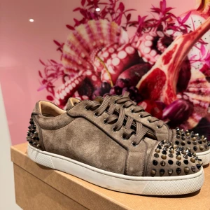 Bruna Louboutin sneakers med nitar - Snygga och exklusiva Louboutin-sneakers i brun mocka med svarta nitar framtill och bak. Klassisk röd sula, bekväm passform och lyxig design. Använda sparsamt och i mycket fint skick. Storlek UK 9, EU 43. Levereras med allt OG 