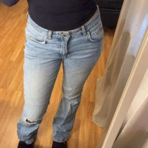 Ljusblå raka jeans med slitning - Säljer ett par ljusblå jeans med rak passform och klassisk femficksdesign. Jeansen har en snygg sliten detalj med hål på ena knät och är tillverkade i jeansmaterial. Perfekt för dig som gillar en avslappnad och trendig stil.