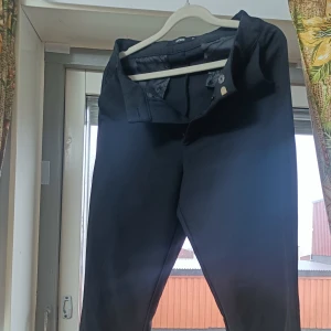 Svarta kostymbyxor från BikBok - Snygga svarta kostymbyxor från BikBok i klassisk rak modell. Byxorna har knäppning fram och är tillverkade i ett mjukt tyg som ger en stilren look. Perfekta för dig som vill ha en clean och enkel stil.