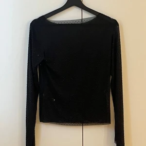 Svart mesh topp med glitterprickar - OBS(En genomskinlig tröja, har en tröja under ),Säljer en svart mesh topp med lång ärm och glittriga prickar över hela tyget. Toppen är tight och genomskinlig, perfekt att styla lager på lager. Rund halsringning och stretchigt material som sitter snyggt på kroppen.