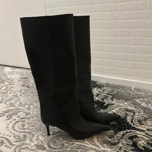 Svarta stövlar med spetsig tå och klack - Säljer ett par svarta höga stövlar med spetsig tå och smal klack. Stövlarna är tillverkade i slätt skinn och har en elegant, stilren design som ger en cool vibe. .