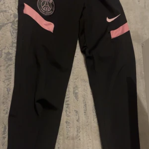 Svarta PSG Nike mjukisbyxor S - Svarta mjukisbyxor från Nike och PSG med rosa detaljer och logga på benet. Byxorna har elastisk midja med snörning och är gjorda i mjukt material som passar chill och sport. Snyggt tapered snitt och coola rosa Nike- och PSG-emblem. Finns inte längre och köpa så rekommenderar verkligen, har aldrig haft på mig de!! Psg byxor 