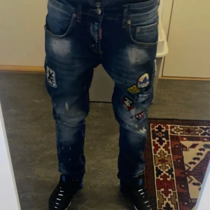 Blå Dsquared jeans med patches och slitningar - Säljer ett par blå Dsquared jeans med coola patches och slitningar framtill. Jeansen har en klassisk femficksmodell och tydliga tvättade detaljer både fram och bak. Passar dig som gillar streetstyle och vill sticka ut lite extra.