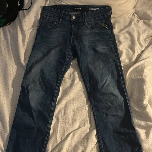 Replay Anbass blå jeans herr - Snygga blå Replay Anbass jeans med klassisk femficksdesign och diskreta slitningar. Jeansen har raka ben, normal passform och är tillverkade i mjukt denimtyg. Perfekta för dig som gillar stilrena och bekväma jeans med en modern touch. W29 L29