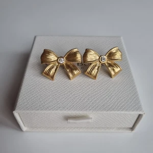 Guldiga rosettörhängen 18k guldpläterad  - Supersöta örhängen i form av rosetter i guldig metall med en glittrande strass i mitten. De har en snygg struktur och detaljerade kanter som ger en lyxig känsla. Perfekta för att lyfta vilken outfit som helst med en söt och trendig touch. Lådan ingår ej.