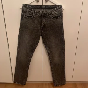 Gråa jeans - Säljer ett par svart/gråa jeans från Jack & Jones, modell Clark Regular. Jeansen har ett fläckigt tyg så dom ser lite annorlunda ut. Använda en gång. Storlek 30/32
