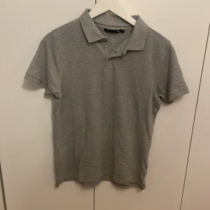 Grå pikétröja  - Grå pikétröja från 157 med krage och knappar framtill. Tröjan är i storlek M men är mindre i storleken och passar dom med xs och s. 