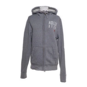 Grå hoodie från Hollister med foder - Mysig grå hoodie från Hollister med vit teddyfoder på insidan. Tröjan har dragkedja, snörning i huvan och två stora fickor framtill. Broderad Hollister-logga på bröstet. Perfekt för kyliga dagar och chill vibes.