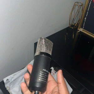 Nikabe Kondensatormikrofon - Nikabe kondensatormikrofon i svart med metallgaller, perfekt för inspelning och streaming. Mikrofonen ser ut att vara i gott skick utan synliga repor eller skador. Levererar klar och professionell ljudkvalitet. Komplett med anslutning för enkel installation.
