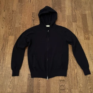 Mörkblå hoodie med dragkedja från Sayless - Mörkblå stickad hoodie med hel dragkedja framtill och huva med snörning. Tröjan har långa ärmar, ribbade muddar och två fickor på framsidan. Perfekt för chill dagar och enkel att matcha med jeans eller joggers.