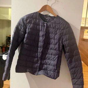 Mörkblå quiltad dunjacka Uniqlo - Snygg mörkblå quiltad dunjacka från Uniqlo med rund hals och tryckknappar framtill. Jackan är lätt och har lång ärm, perfekt för kyliga dagar. Enkel och stilren design som funkar till många outfits.