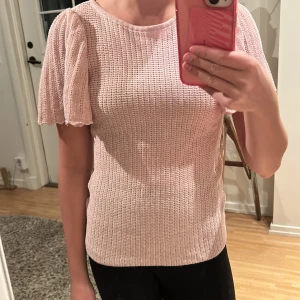Ljusrosa stickad topp med puffärm - Supersöt ljusrosa stickad topp med korta volangärmar och rund hals. Toppen har ett ribbat mönster och är tillverkad i ett mjukt stickat material som ger en skön känsla. Ärmarna har vågiga kanter för extra detalj. Glittriga detaljer i tröjan. Perfekt för dig som gillar något litet extra💗Vet ej storlek eller märke då lappen i tröjan är borta men passar XS-S