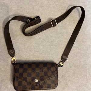 Brun axelväska - Snygg axelväska i klassiskt brunt rutigt mönster med justerbar axelrem och guldfärgade metalldetaljer. Perfekt storlek för det viktigaste och en ikonisk design. Obs! Rummet har gått av. Se bild 2