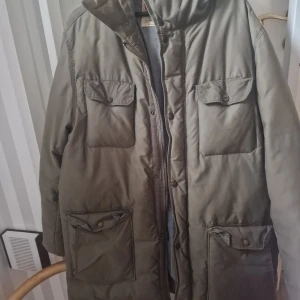 Olivgrön vinterjacka från Levi's XL - Vinterjacka från Levi's i olivgrön färg med huva, fyra stora fickor med lock och knappar samt dragkedja framtill. Jackan har en loose passform och är fodrad med grått tyg på insidan. Perfekt för kalla dagar och har en clean, urban look. Material: Polyamid 39%, Dun 40%, Bomull 61%.  Jackan är naturligtvis använd, men välvårdad och fin!
