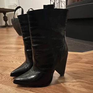 Spetsiga boots  - Säljer ett par svarta boots med krokodilpräglat mönster och spetsig tå. Skorna har hög klack och är tillverkade i skinnimitation med glansig finish. Aaas snygga men lite för små för mig!!💕💕😭