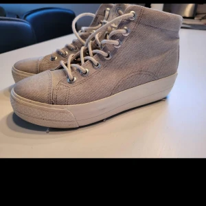 Beige höga sneakers Vagabond strl 36 - Snygga höga sneakers från Vagabond i beige canvas med vita snören och platt sula. Skorna har rund tå och metallöglor för snörningen. Perfekt för dig som gillar enkel och stilren design med lite extra höjd på sulan.
