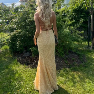 Gul maxiklänning  - Superfin gul maxiklänning från showpo storlek 36 med blommigt mönser, fyrkantig urringning och snörning i ryggen. Klänningen är mermaid figur och tajt passform upptill och utsvängd nertill, perfekt för sommarens speciella tillfällen. Skräddar sydd på sidan ungefär 2-3 cm för den skulle bli lite tajtare. Matrialet är inte stretch. Är 170 cm lång för preferens och den har lite smuts längst ner men försvinner när den tvättas. 