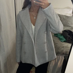 Grå skepparkavaj XS - Snygg grå skepparkavaj i klassisk modell med bred krage och dubbelknäppning. Jackan har en rak passform och är tillverkad i mjukt ullmaterial. Perfekt för dig som gillar stilrena och tidlösa plagg. Storlek XS, passar dig som vill ha en lite mer fitted look. Jackan är helt oanvänd med prislappen kvar! 💖💖