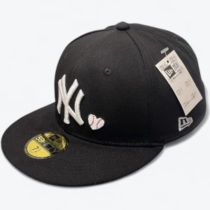 Svart New Era Yankees keps 59FIFTY 7 3/4 61.5 cm  - Svart New Era 59FIFTY keps med New York Yankees broderat i vitt framtill och ett litet hjärta bredvid. På sidan finns en färgglad World Series 1996 patch. Platt skärm med grå undersida och klassisk New Era-logo broderad på sidan. Snygg och sportig look.