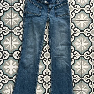 Blå bootcut jeans med stora fickor - Snygga blå jeans med bootcut passform och stora fyrkantiga framfickor. Jeansen har dubbla knappar i midjan och klassiska bakfickor. 