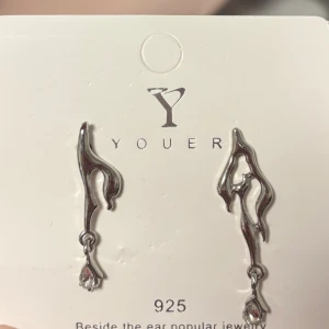 Silvriga örhängen från Youer -  silvriga örhängen från Youer i abstrakt, vågig form med hängande droppformad detalj längst ner. 