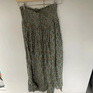 Zara kjol - Säljer en bohemisk långklänning med blommigt mönster i grönt och beige. Kjolen har en smockad överdel och ett flowy fall, perfekt för dig som gillar avslappnad och snygg stil. Materialet känns lätt och luftigt, idealiskt för varmare dagar.