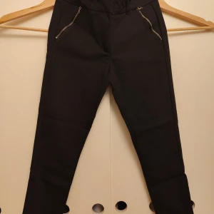 Svarta tapered byxor Soyaconcept - Svarta byxor från Soyaconcept med tapered passform och hög midja. Snygga detaljer med dragkedjor vid fickorna framtill och diskreta bakfickor. Materialet är en mix av bomull, polyamid och elastan för skön stretch. Perfekt för dig som gillar stilrena och bekväma byxor.