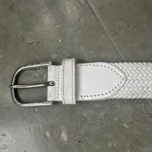 Vitt flätat bälte med silverfärgat spänne - Snyggt vitt bälte med flätad struktur och silverfärgat metallspänne. Bältet har detaljer i vitt skinn vid spännet och är perfekt för att ge en clean och fräsch touch till din outfit. Passar dig som gillar stilrena accessoarer med lite extra textur. 