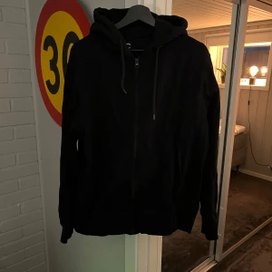 Svart hoodie med dragkedja - Svart hoodie med huva och snörning, hel dragkedja framtill och långa ärmar. Perfekt för chill dagar och enkel att matcha med jeans eller joggers. Mjuk och skön känsla tack vare bomullsmaterialet. Det är en XL men känns som en L.
