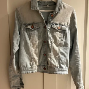 Ljusblå jeansjacka från Noisy May - Snygg ljusblå jeansjacka från Noisy May i klassisk modell med bröstfickor och kopparfärgade knappar. Jackan har lång ärm, rak passform och är tillverkad i mjukt jeanstyg. Perfekt att slänga över en hoodie eller t-shirt för en chill look.