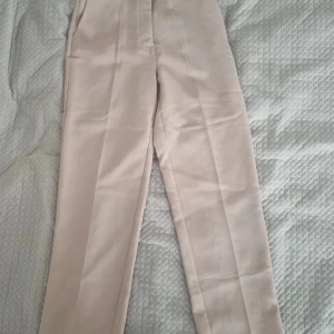 Beiga kostymbyxor med raka ben - Snygga beiga kostymbyxor med raka ben och pressveck. Byxorna har hällor för bälte. Materialet känns mjukt och har en lätt stretch. Har bara använt några gånger 