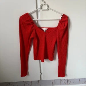 Röd ribbad offshoulder topp H&M  - Säljer en snygg röd ribbad topp från H&M i storlek XS. Modellen är offshoulder med långa ärmar och har en croppad passform. Materialet är mjuk och stretchig bomull, perfekt för dig som gillar trendiga och bekväma plagg med lite edge.