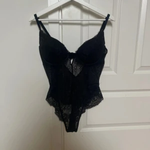 Svart spets body - Säljer en svart body med genomskinlig spets och snygga detaljer. Den har justerbara axelband, v-ringad front. Spetsen har ett diskret mönster och ger en lyxig känsla. Perfekt för dig som vill ha något extra till din outfit.