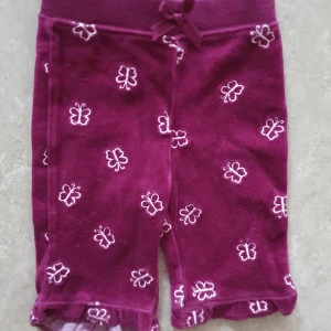 Shorts - Säljer ett par söta mörklila shorts från KappAhl med broderade vita fjärilar över hela tyget. De har en hög midja med rosett framtill och volangkant vid bensluten. Materialet är mjukt och känns som bomull, perfekt för chill dagar.