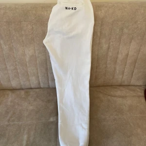 Vita mjukisbyxor från NA-KD - Säljer ett par vita mjukisbyxor från NA-KD med resår och snörning i midjan. Byxorna har fickor på sidorna och en bakficka med broderad NA-KD-logga. Perfekta för en chill och avslappnad stil.