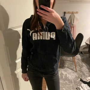 Svart hoodie från Puma med dragkedja - Svart hoodie från Puma med stor vit logga framtill. Tröjan har huva, dragkedja och fickor på magen. Jag skulle gissa att storleken är mellan XS-S då de står att den är XL på tröjan vilket ja inte tror stämmer