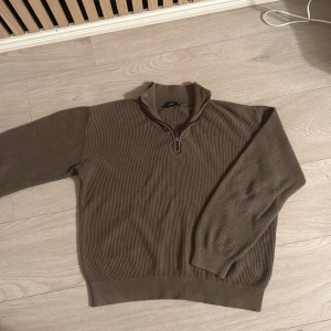 Brun stickad half zip tröja  - Snygg brun stickad tröja  i storlek XS. Tröjan har en ribbad struktur och en praktisk half zip-dragkedja vid kragen. Perfekt för lager-på-lager och chill stil. Långärmad och med breda muddar vid ärmslut och nederkant.