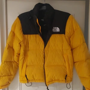 Gul och svart pufferjacka North Face - Säljer en fet gul och svart pufferjacka från The North Face. Jackan har hög krage, dragkedja och snörning nedtill. Fylld med dun och har två sidofickor med dragkedja. Perfekt för kalla dagar och har en riktigt clean look.